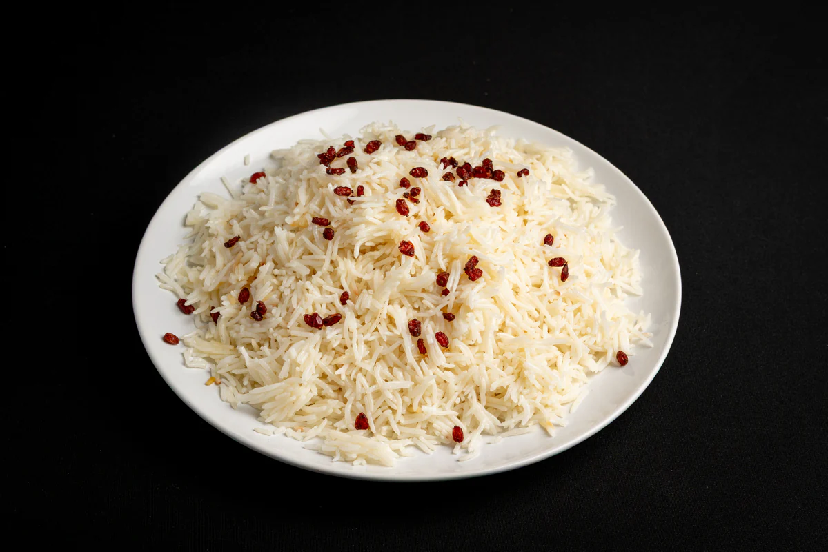 A mound of plain steamed basmati on a white plate, scattered with dried red barberries.