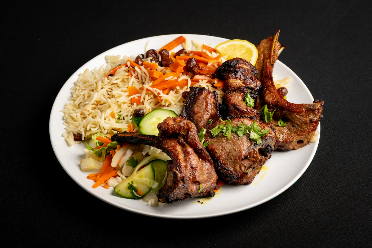 Three charred lamb chops on the bone beside pulao rice, with cucumber, carrot and a slice of lemon.