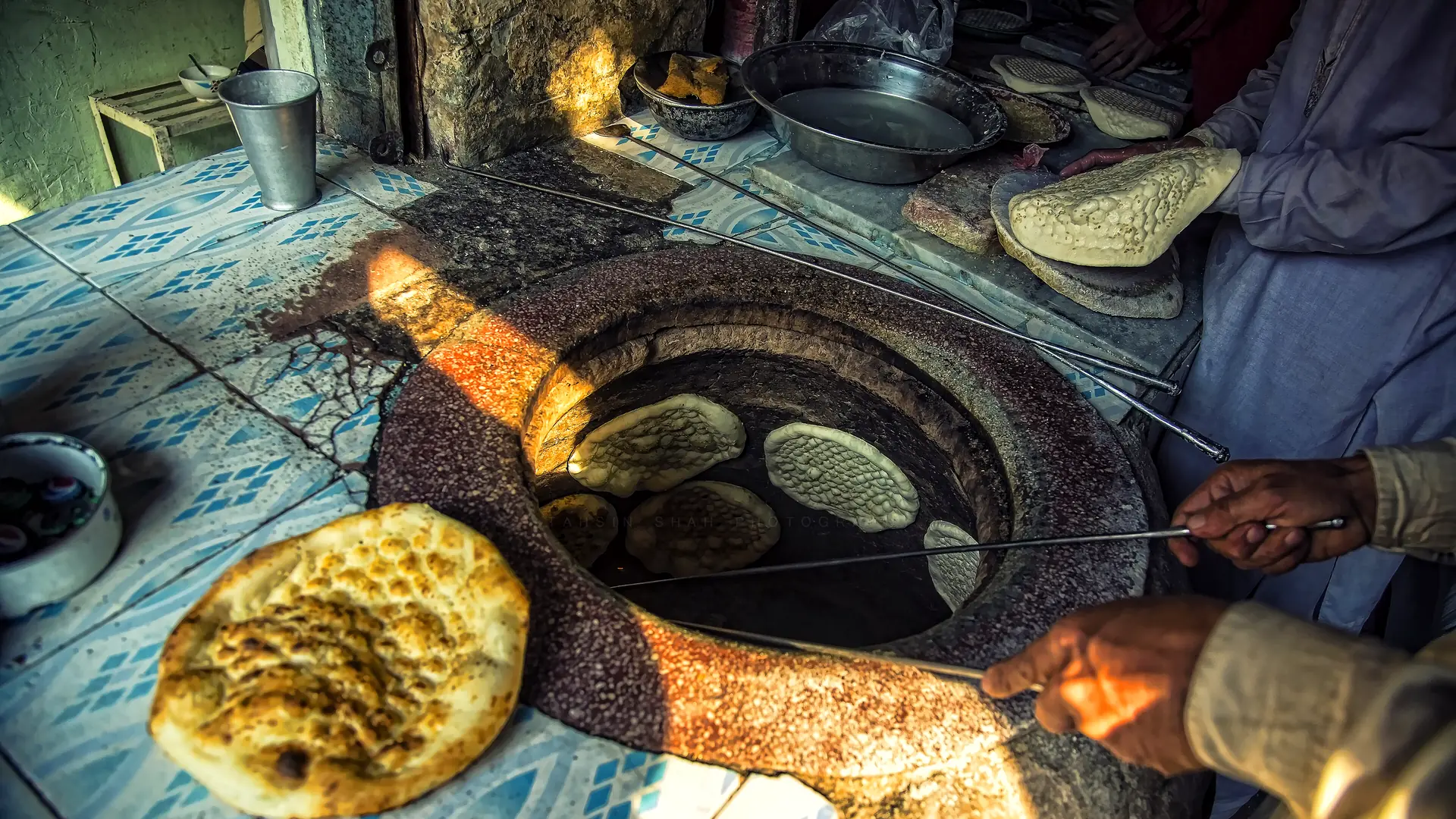 Hands lifting golden flatbreads from the mouth of a glowing clay tandoor.